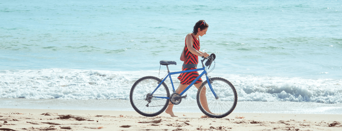 Femme poussant son vélo sur la plage tout au bord de la mer